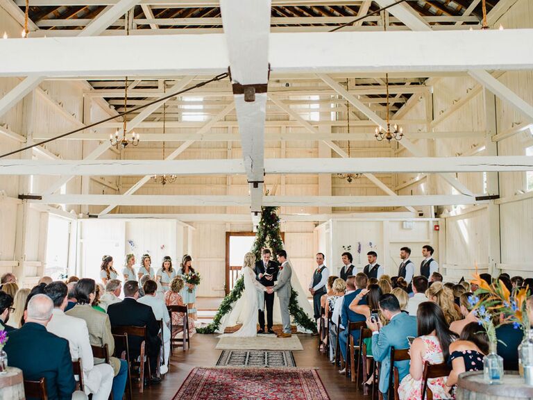 Bride and groom saying vows in barn wedding ceremony in front of modern angular green ceremony backdrop