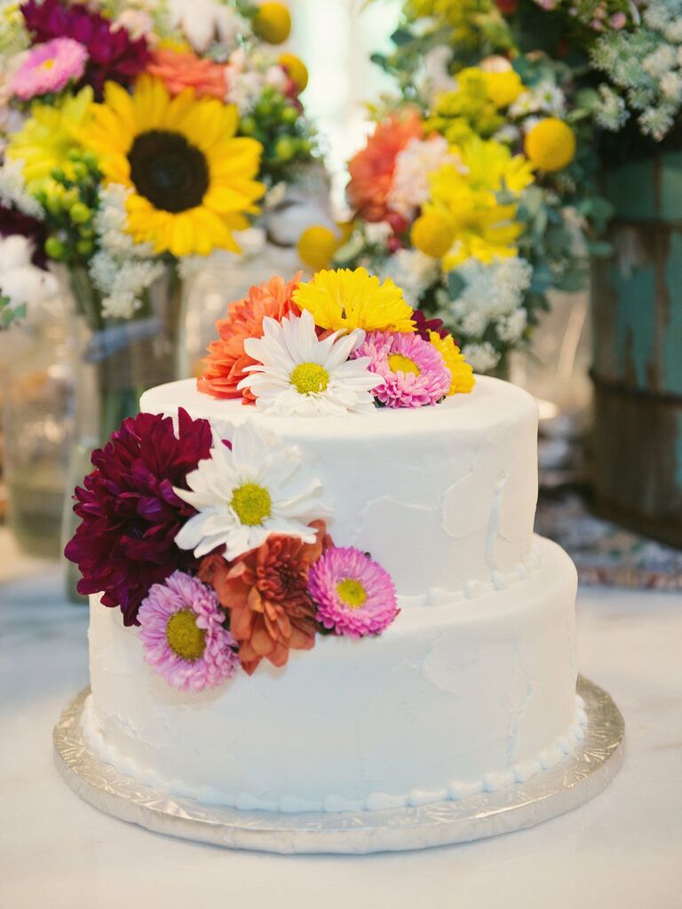 two tier buttercream wedding cake decorated with pink, yellow, orange and red mums