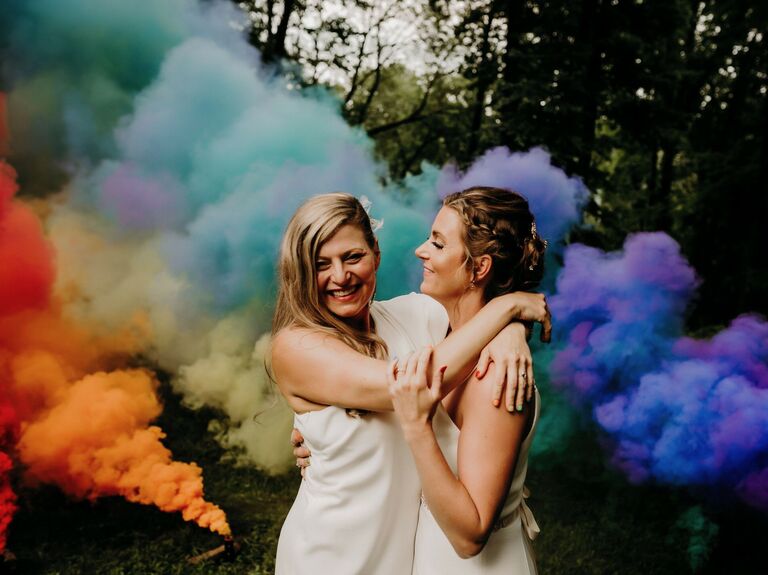 Two brides pose amongst rainbow smoke