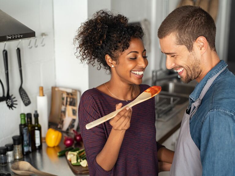 Couple smiling tasting homemade sauce in kitchen, cooking class gift for wife