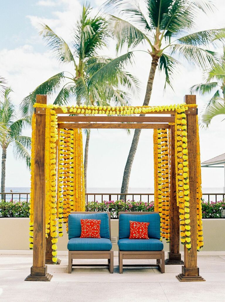 outdoor Indian wedding ceremony mandap decorated with yellow marigolds flowers garlands and bright blue upholstered chairs