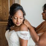 Friend helping bride put on her wedding day necklace