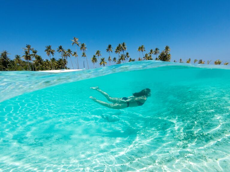 A woman swims through the crystal clear water of the Maldives.