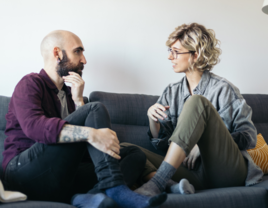 couple sitting on a couch talking with eachother, how to talk about mental health and boundaries with your partner