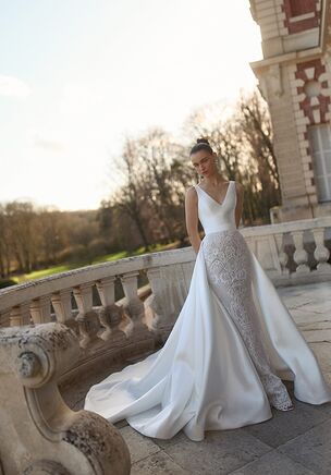 Lustrous Mikado fabric paired with dimensional lace creates a striking visual statement in the Kaori gown from WONÃ Concept. Clean lines define the structured trumpet silhouette, which hugs the body before dropping to a floor-length hem. Framed by a sleeveless V-neckline, the light ivory bodice features delicate floral motifs. An open, low-cut back balances the frontend. A detachable overskirt alters the volume of the skirt. The train sweeps backward for an architectural presentation.