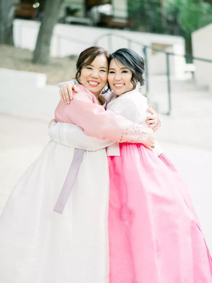 Bride and mom wearing hanboks for Korean wedding and sharing a hug