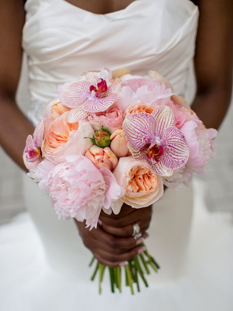 A bride holds a bouquet of peachy peonies and purple-striped orchids.