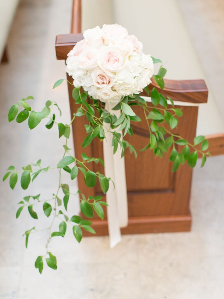 classic wedding aisle marker tied to church pew with white and blush roses, greenery vines and long pink ribbons, 