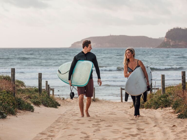 A couple holding surfing boards on a beach in Sydney, Australia.