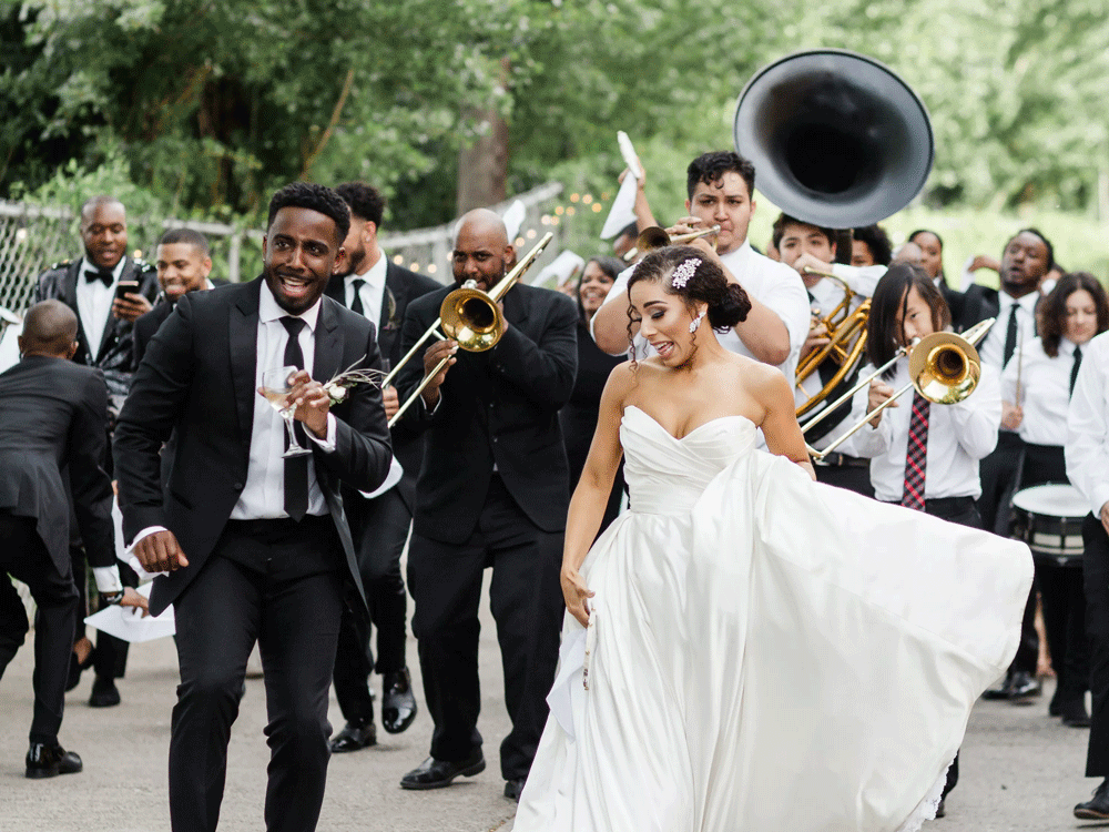 Bride and groom dancing with New Orleans wedding parade behind them.