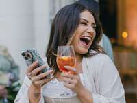 Woman holding drink and phone in her hands while laughing 
