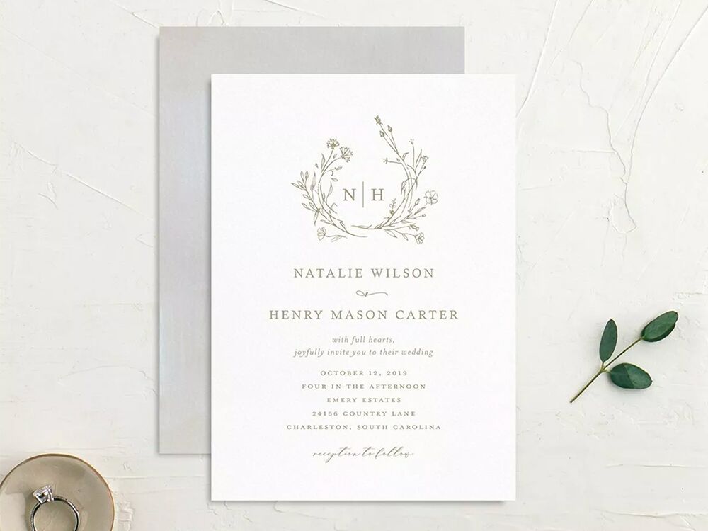 Monogram framed by greenery above event details with classic gray type on white background