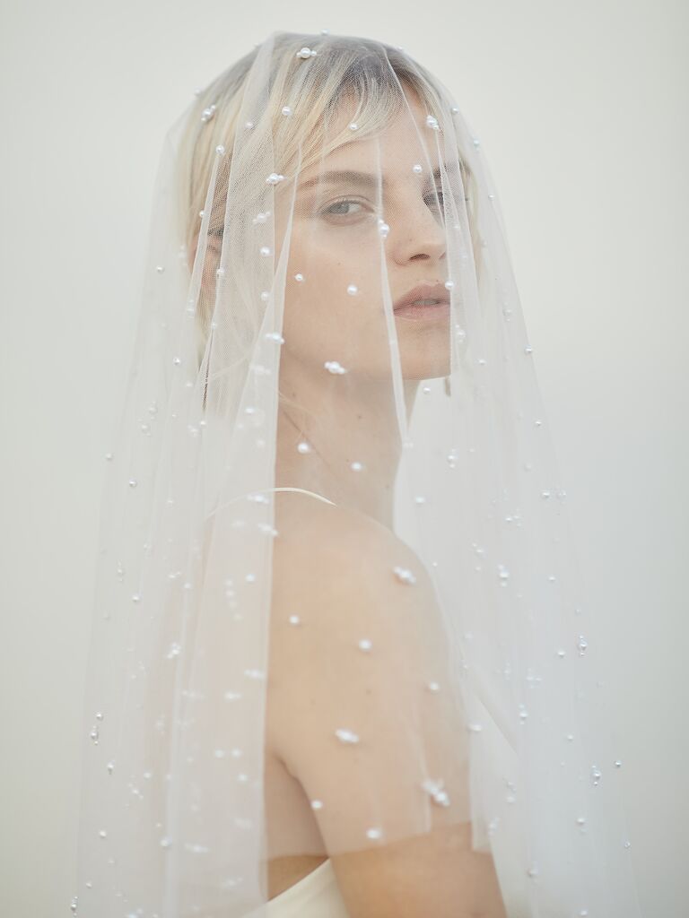 Model wears sheer mid-length veil with pearl embellishments. 