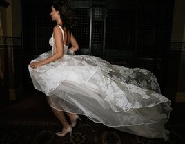 Model runs while a white floral wedding gown billows behind her. 