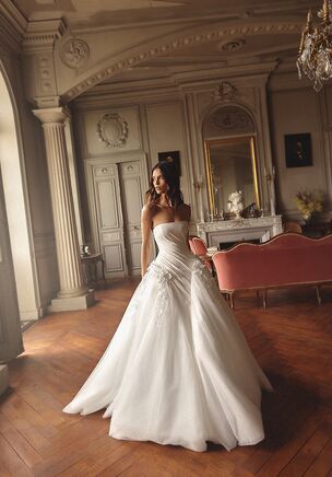 Veneto gown is a magnificent off-shoulder princess ball gown designed to create a truly fairytale bridal look. The corset is crafted from structured suiting fabric with elegant draping and fastens with a zipper at the back, beautifully shaping and defining the waistline. The voluminous skirt is made of soft layers of tulle with multiple linings for fullness and movement. The waist is adorned with handcrafted 3D flowers and appliqués that cascade gracefully from the waist down the skirt, creating a breathtaking decorative flow. A long, sweeping train completes the look with regal drama and timeless romance. Veneto gown is perfect for brides who dream of a classic, luxurious princess silhouette with exquisite handmade detailing.