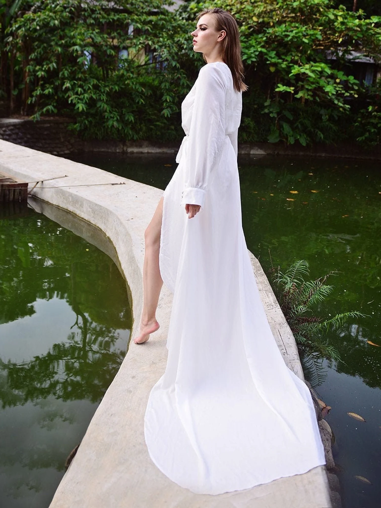 A model stands on a stone path over a pond, wearing this glamorous Maxi Bridal Robe With Train.