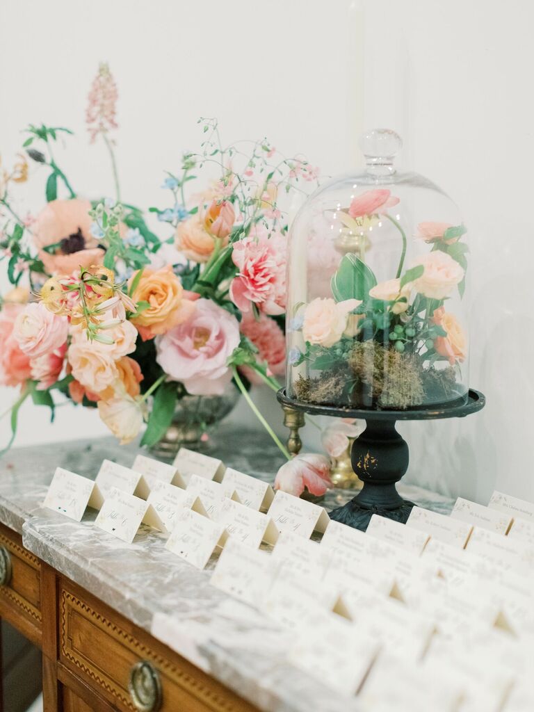 Escort card display with cloche-covered floral arrangement