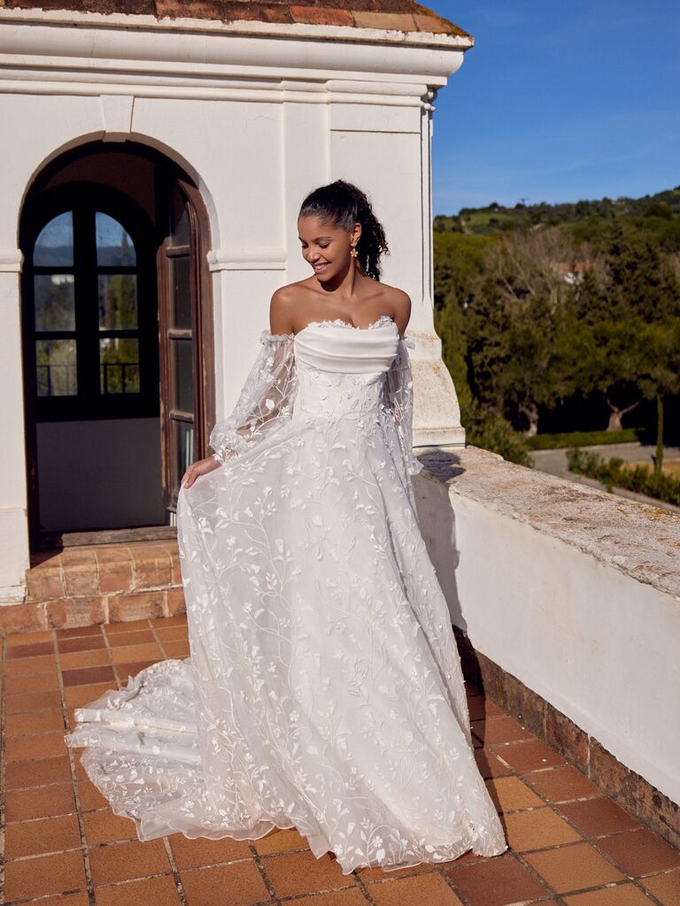Off-the-shoulder wedding dress by Lillian West with sheer sleeve and 3D floral embroidery