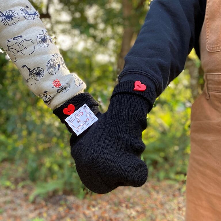 Couple holding hands wearing matching black mittens with red heart button