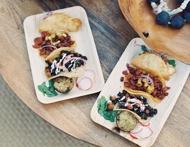 Two rectangular plates of assorted tacos garnished with lime, cilantro, and radishes. 