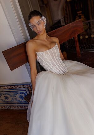 A sophisticated gown featuring an elongated corset with lace-up closure, adorned with minimalist 3D lace for a delicate yet modern touch. The voluminous tulle skirt is enhanced with layers of creamy mesh, adding depth and airiness to the silhouette. This gown is designed without a train, making it both elegant and practical for effortless movement.