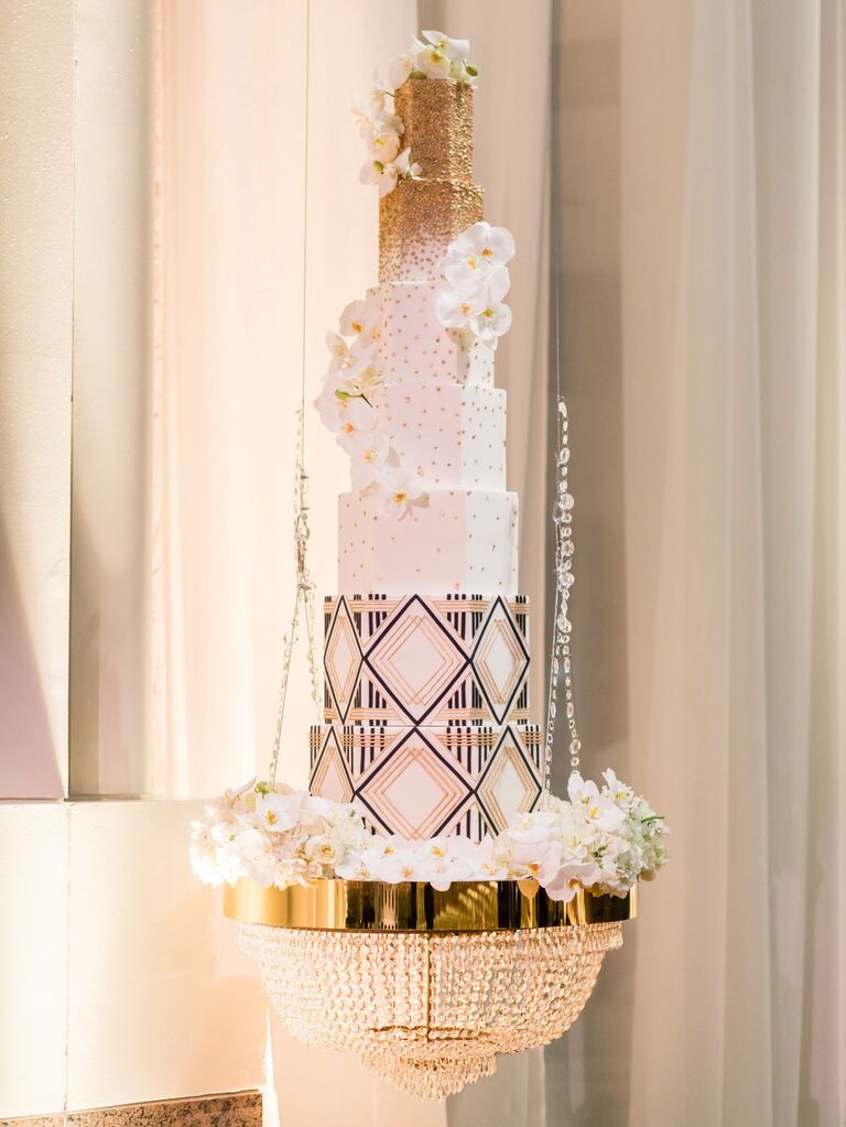 luxe new year's eve wedding cake hanging from a crystal chandelier with gold and black art deco designs on each tier of the cake