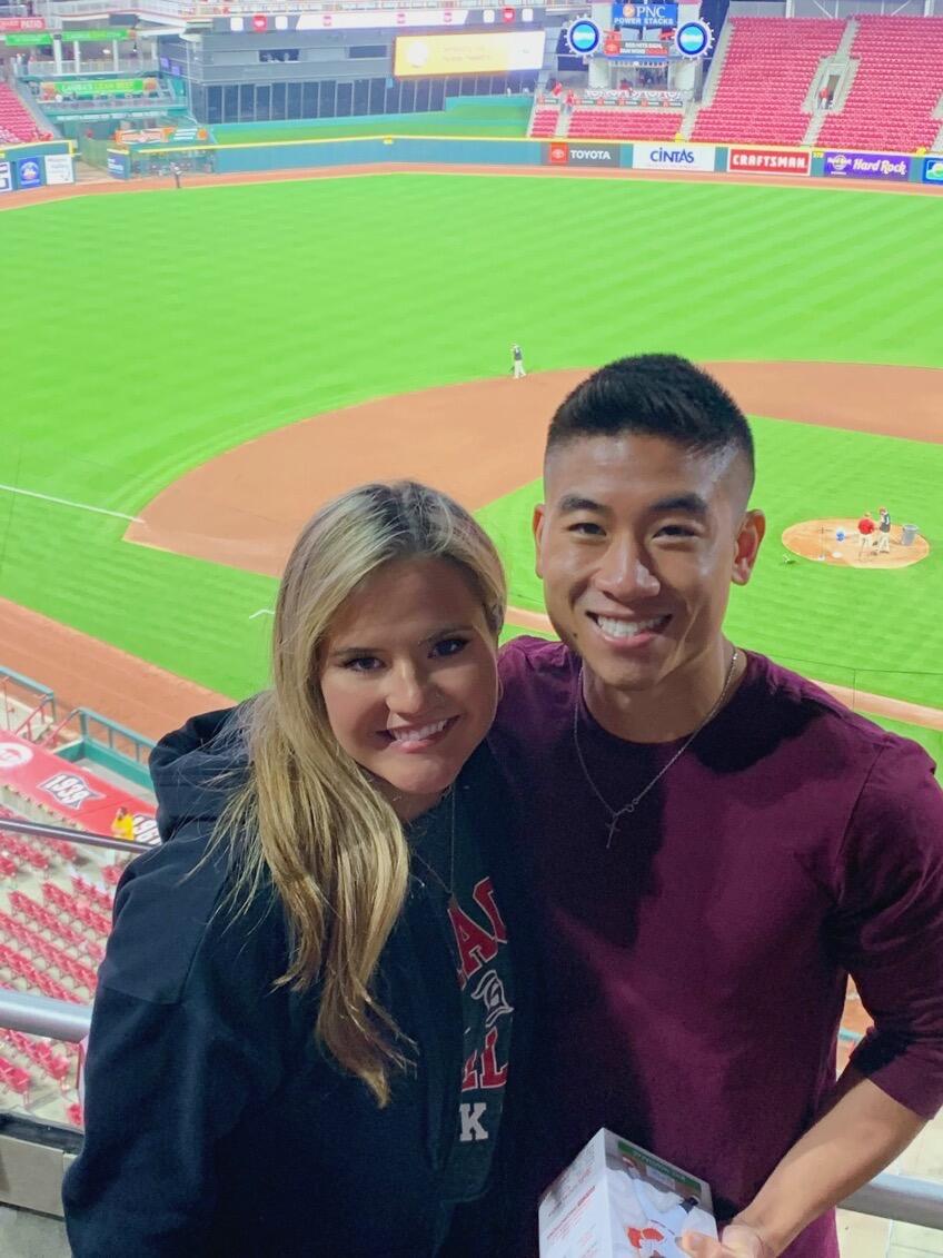 Sarah & Joseph met in Cincinnati, Ohio in the fall of 2020 when Joseph was working on his last year of pharmacy residency and Sarah began her graduate studies.   The two were both new to the city and found it challenging to meet new people due to the aftermath of the Covid-19 pandemic.  They connected online in hopes of finding a friend they could explore and adventure with.  Their first date was eating pizza and going to a haunted house.  The next week, they went on another date and continued to do so weekly for the next three and a half years!  

While Joseph diligently worked long hours during his residency, the two would often resort to cooking dinner together and walking outside, exploring the city.  Pictured is Sarah & Joseph at a Cincinnati Red's game.