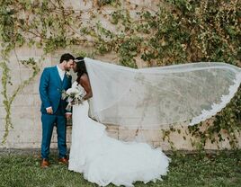 bride wearing cathedral wedding veil with lace trim stands next to groom as wedding veil lifts in the breeze