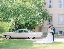 Couple posing for a picture beside the vintage wedding car and venue