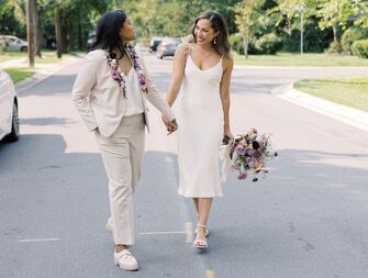 candid photo of same-sex couple featuring two brides walking down the street holding hands