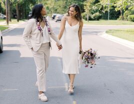 candid photo of same-sex couple featuring two brides walking down the street holding hands