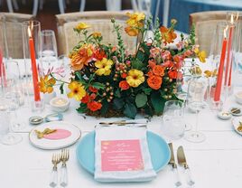 colorful wedding centerpiece idea with yellow, orange and red flowers accented by matching candles and plates
