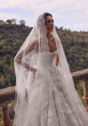 A timeless masterpiece with vintage flair, the Hecate gown is crafted from radiant lace that shimmers delicately with every movement. The bodice features a romantic sweetheart neckline and a sculpted corset that gracefully tapers downward, accentuating the waist. The back laces up for a custom, feminine fit. The skirt flows from the waist into a soft A-line shape, adorned with exquisite 3D floral appliqués that add depth and dimension to the design. A modest train completes the look, giving it an air of graceful nostalgia. Hecate dress is perfect for the bride drawn to old-world charm with a modern twist.