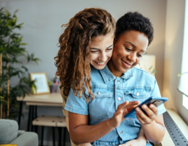 Woman using phone and partner hugging her from behind 