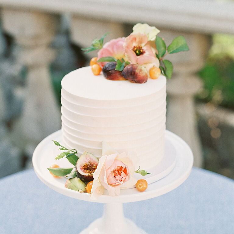 One-tier cake on white cake stand with fresh fruit and flower decorations