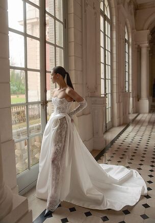 Intricate layers of Chantilly lace and shimmering beading trace the form of the Charleen gown from the WONÃ Concept Maison Blanche collection. The structured bodice features exposed corset detailing and an irregular, lowered waistline that dips dynamically in the front. A sculpted neckline frames the collarbone, balancing a plunging open back. Tailored in a sheath silhouette from smooth Mikado overlaid with floral textures, the gown skims the figure and opens into a high leg slit. Detachable long lace sleeves instantly shift the style from covered to bare-shouldered. Below, the narrow skirt extends into a sweeping chapel-length train trailing softly behind each step.