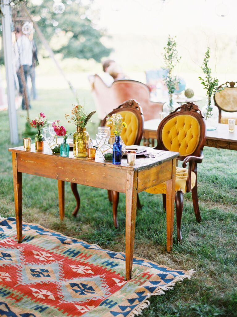 vintage wedding sweetheart table idea with yellow velvet armchairs, vintage glass jars, wooden table and colorful antique patterned rug