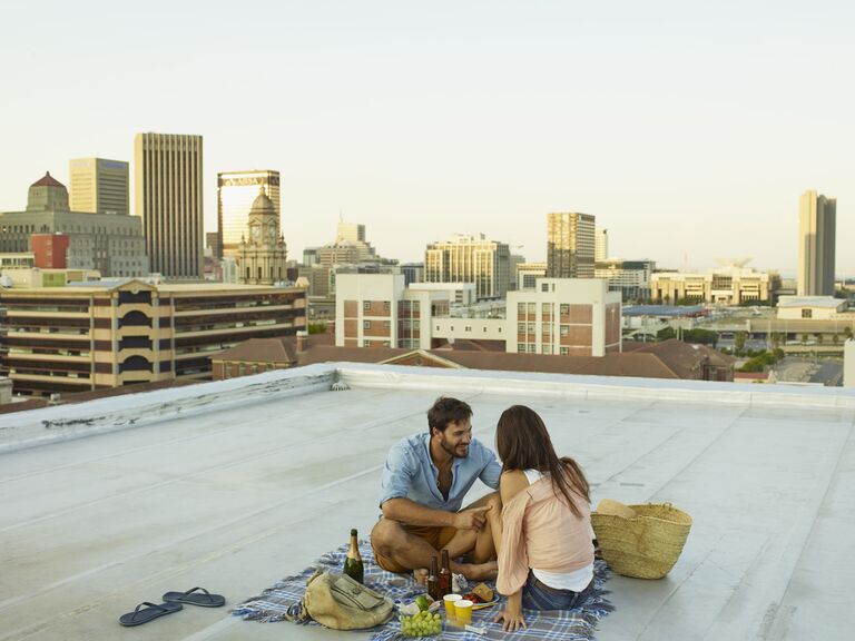 Couple enjoys a picnic meal on a flat rooftop in a downtown area. 