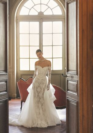 Encore gown is an exquisite mermaid-style dress crafted entirely from delicate lace, designed to celebrate elegance and drama in one look. It features off-shoulder long sleeves and a lace-up corset that beautifully shapes the silhouette. The gown includes a removable overskirt, allowing the bride to choose between a sleek mermaid shape or a grand, voluminous entrance. The signature train is uniquely layered in soft cascades and trimmed with Chantilly lace along the edges, creating a truly captivating effect. Small floral buttons at the waist help secure the train when needed. With multiple underlayers for structure and comfort, Encore gown can be worn with or without the additional overskirt - offering two stunning bridal looks in a single design.