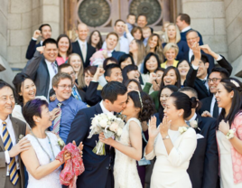 Bride and groom kissing on steps surrounded by friends and family