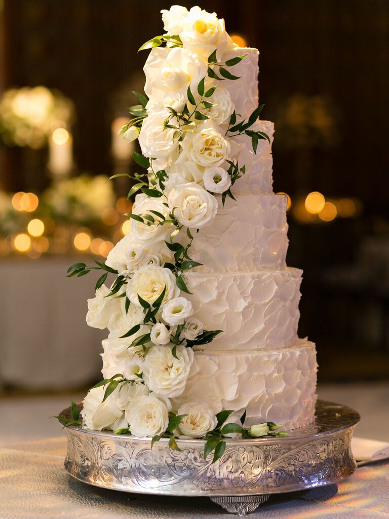 five tier wedding cake with textured buttercream and white roses cascading down the front