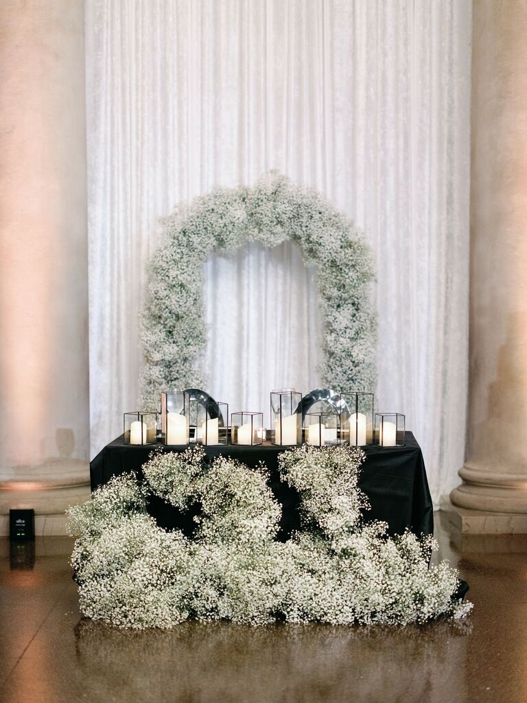 wedding sweetheart table with baby's breath arch backdrop and clusters of baby's breath and white candles in front of the table
