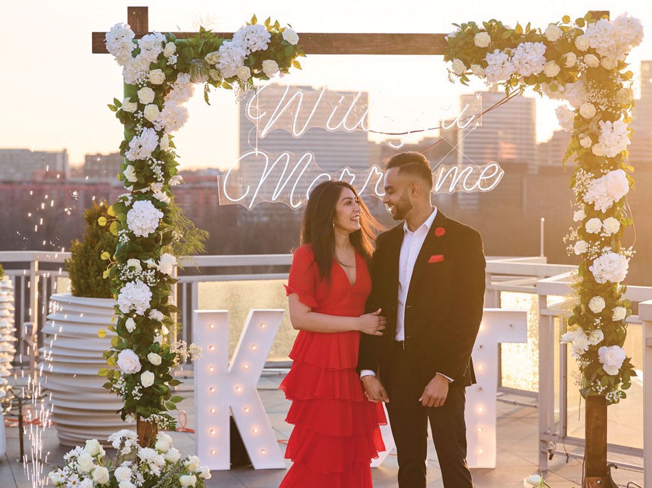 Couple hugging in front of neon 'will you marry me' sign