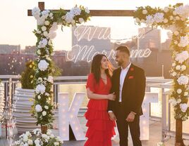 Couple hugging in front of neon 'will you marry me' sign