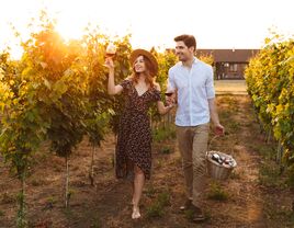 Couple drinking wine and walking through vineyard with picnic basket