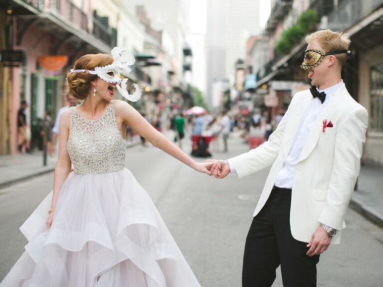 Newlyweds holding hands during second line celebration with mardi gras masks