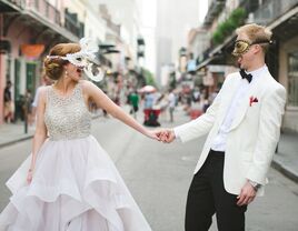 Newlyweds holding hands during second line celebration with mardi gras masks