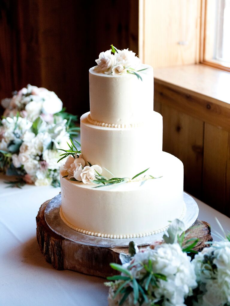 three tier smooth buttercream wedding cake with small white flowers on top and middle tier