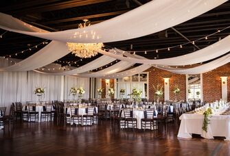 Elegant event space with hanging drapery and bistro lighting with exposed red brick walls and dark wood flooring