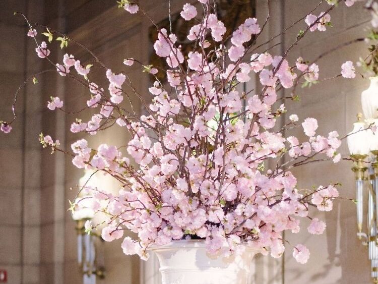 A white urn flower arrangement with flowering cherry blossom branches